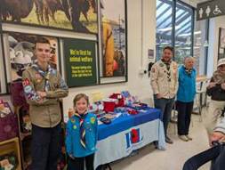 A group of people standing in front of a table with a table with a table with a sign and a child scout

AI-generated content may be incorrect.